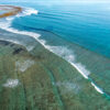 Aerial view of clean reef waves breaking in turquoise ocean water