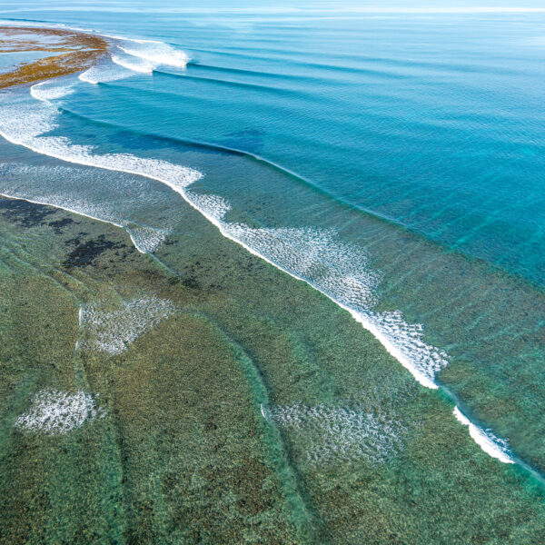 Aerial view of clean reef waves breaking in turquoise ocean water