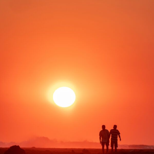 Silhouetted figures walking along the shoreline at sunset
