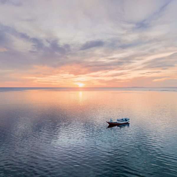 Aerial ocean lifestyle photography showing a traditional fishing boat floating on calm water at sunset in Rote, Indonesia