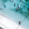 Aerial view of surf taxi boats carrying surfers back to shore in clear turquoise water in a fine art surf lifestyle photograph.