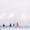Group of surfers sitting on their boards in calm ocean water under a soft cloudy sky