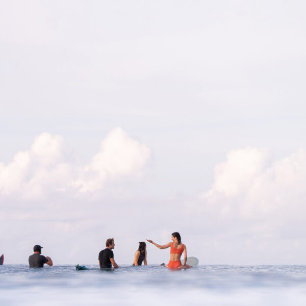 Group of surfers sitting on their boards in calm ocean water under a soft cloudy sky