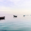 Small wooden boats floating on calm pastel-toned ocean water