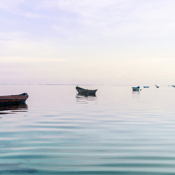 Small wooden boats floating on calm pastel-toned ocean water